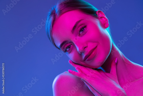 Neon glow. Young adorable girl with well-kept skin and naked shoulders isolated over dark background in pink neon light. Concept of art, fashion, style, inspiration