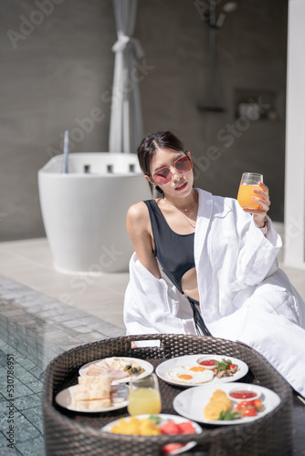 Woman relaxing and eating floating breakfast in the pool on luxury villa.