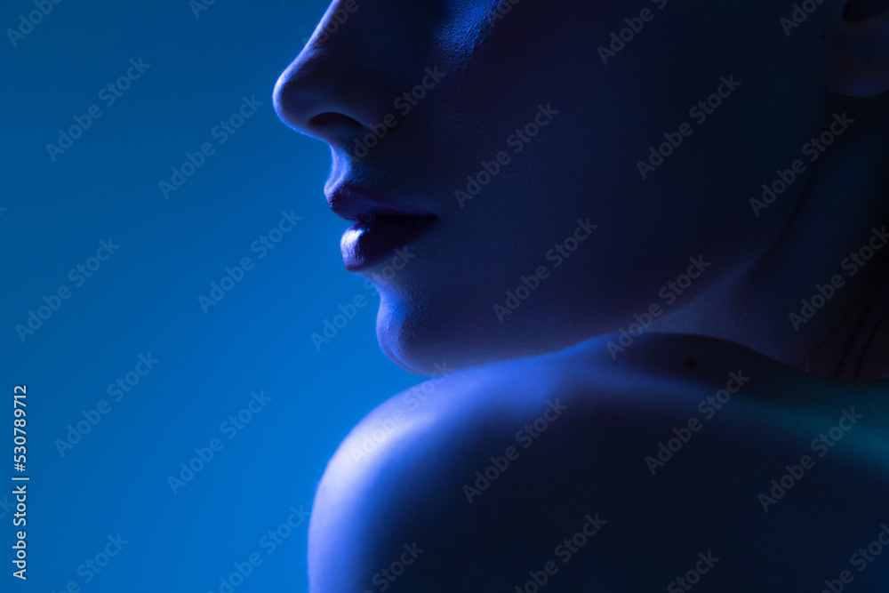 Night life. Cropped image of young woman in neon light on dark blue background. Monochrome. Cyberpunk style, beauty, cosmetics concept.