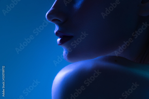 Night life. Cropped image of young woman in neon light on dark blue background. Monochrome. Cyberpunk style, beauty, cosmetics concept.