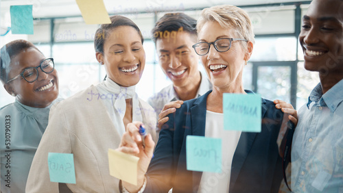 Teamwork, planning and strategy with a business woman, manager or CEO working with a team on a glass wall and sticky notes. Collaboration, learning or development with a group in an office for growth