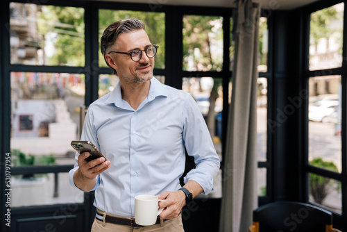 European grey man drinking coffee and using cellphone outdoors