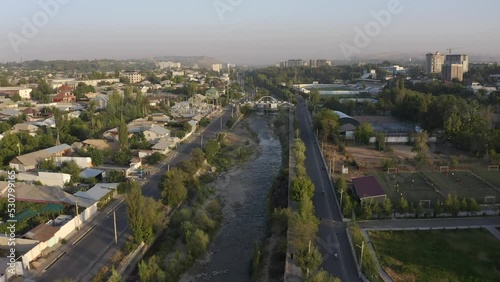 Aerial view of the city of Osh, Kyrgyzstan. Panorama of an Asian city at sunset. View of roads, cars, roofs of houses, a dried-up river, trees.