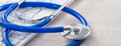 Blue stethoscope on laptop computer keyboard, medical design concept.