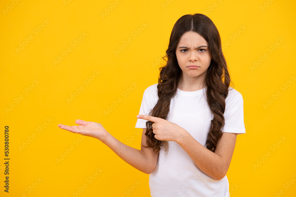 Close up portrait of teenager child girl showing at copy space, pointing to ads advertising, isolated over yellow background. Unhappy sad teenager girl. Close up portrait of teenager child girl showing at copy space, pointing to ads advertising, isolated over yellow background. Unhappy sad teenager girl.