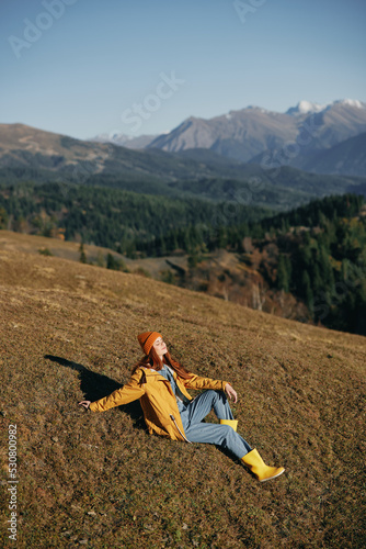 Woman sitting full-length on a hill and looking at the mountains happy nature trip on a hike in the fall, freedom lifestyle on the move