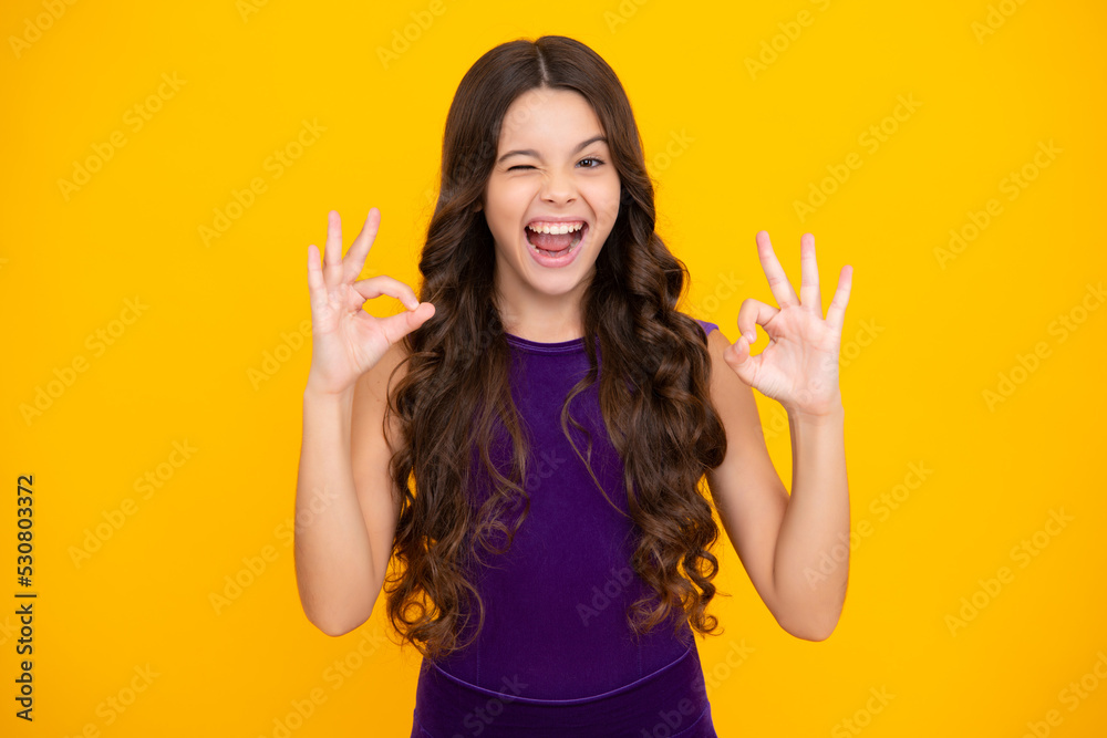 Emotional portrait of caucasian teen girl. Funny teenager making ok gesture and winking on yellow background. Child laughing looking very happy. Excited face, cheerful emotions of teenager girl. Emotional portrait of caucasian teen girl. Funny teenager making ok gesture and winking on yellow background. Child laughing looking very happy. Excited face, cheerful emotions of teenager girl.