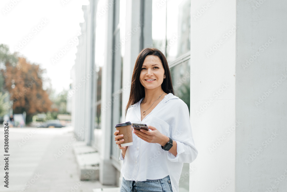 Street portrait of a young woman with a phone in her hand and a coffee to go