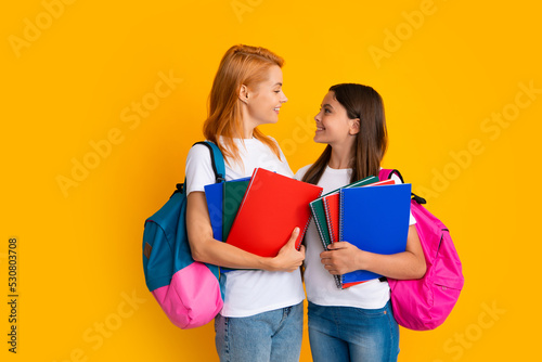 Mother and daughter schoolgirls with school bag ready to learn. Back to school. Mom and child on isolated yellow studio background. Family education. photo