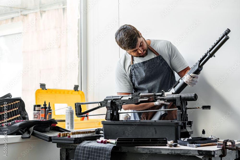 Close up of young man in apron disassembling a gun above the table Close up of young man in apron disassembling a gun above the table