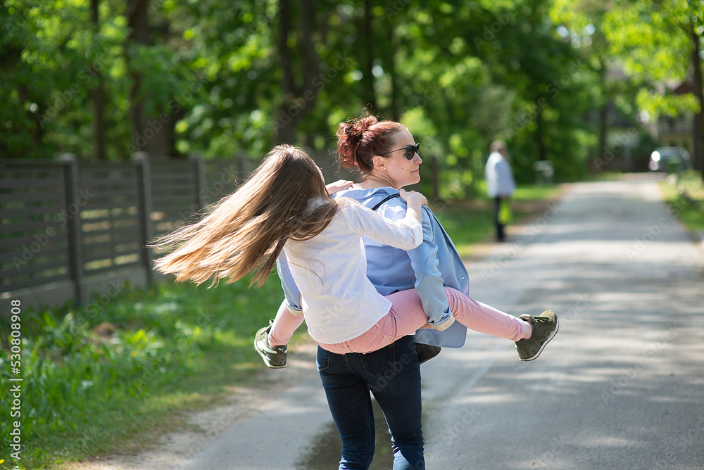 Obraz premium Rear view on young daughter on a piggy back ride with her mother.Happy family having fun outdoor