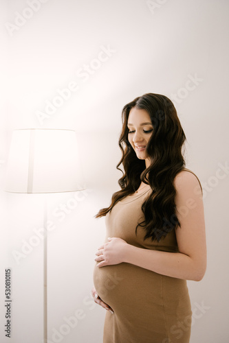 Beautiful pregnant girl with curls in a dress in a bright studio with a stylish interior, the concept of a happy pregnancy and family