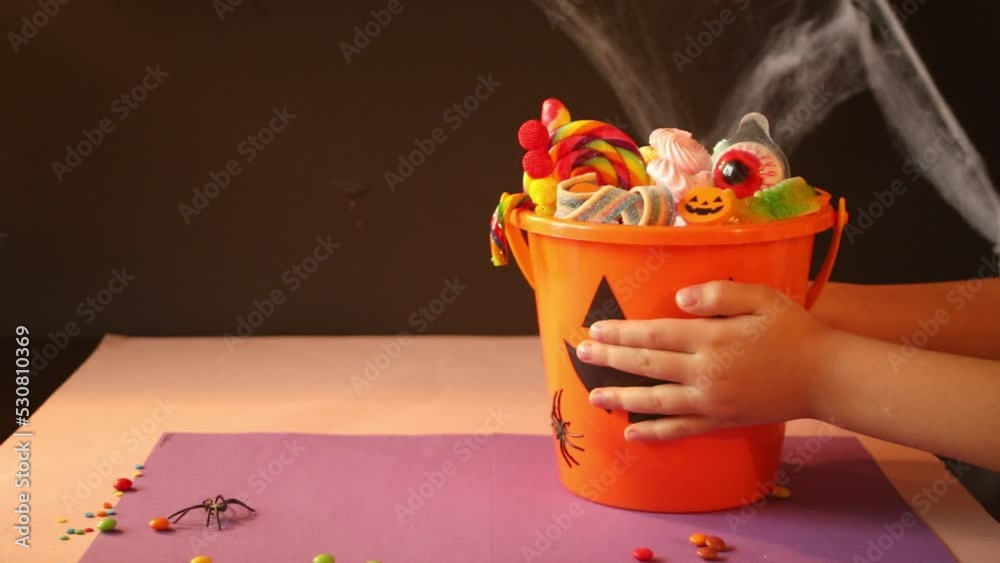 Child kid hands take Halloween Jack o Lantern orange bucket with candy.