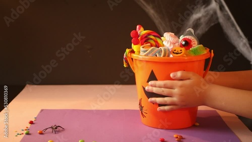 Child kid hands take Halloween Jack o Lantern orange bucket with candy.