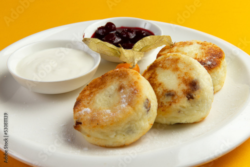 Traditional breakfast syrniki in a plate on a yellow background.