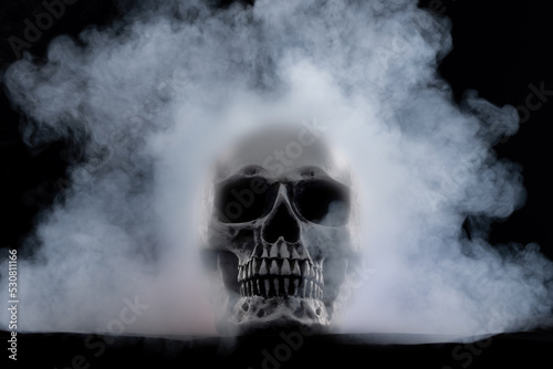 Halloween human skull on an old wooden table over black background. Shape of skull bone for Death head on halloween festival which show horror evil tooth fear and scary with fog smoke, copy space