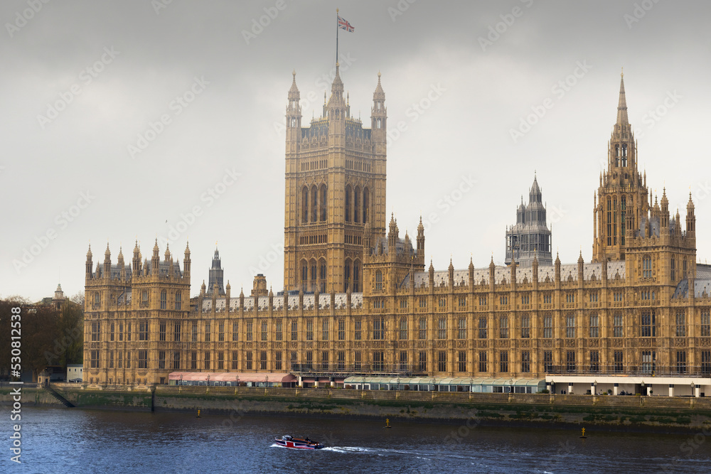 London house of parliament in a winter troubled weather while a UK boat passing by in the river in front of the great building. London house of parliament in a winter troubled weather while a UK boat passing by in the river in front of the great building.