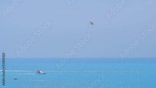 Multicolor parachute is hiding behind the boat. Parasailing, active form of recreation. A sailboat, a speedboat, a jet ski, a catamaran sailing on the blue sea leave white traces behind them.