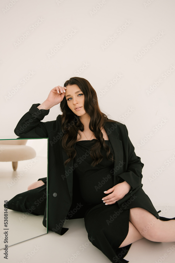 Beautiful pregnant girl with curls in a black dress on a white background, the concept of a happy pregnancy and family Beautiful pregnant girl with curls in a black dress on a white background, the concept of a happy pregnancy and family