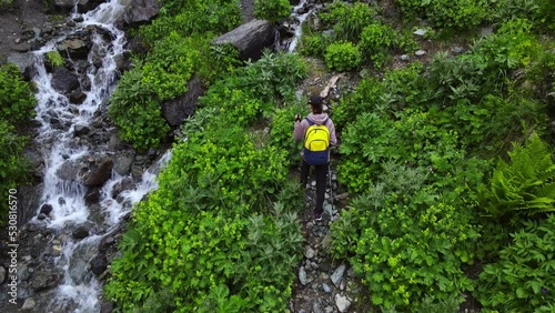 Young female traveler hiking along rapid creek in the mountains, aerial tracking shot photo