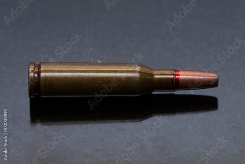 a cartridge with a bullet with an offset center lies on a dark background, selective focus, reflective surface. Concept:prohibited expansive bullets, the war in Ukraine.