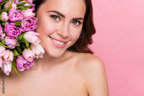 Photo of adorable shiny young woman naked shoulders holding flowers blossom empty space isolated pink color background