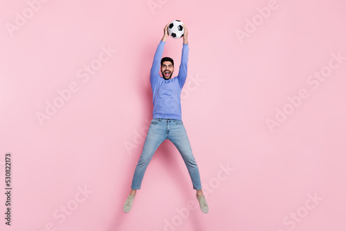 Full length photo of strong funny guy dressed blue pullover jumping high catching ball isolated pink color background