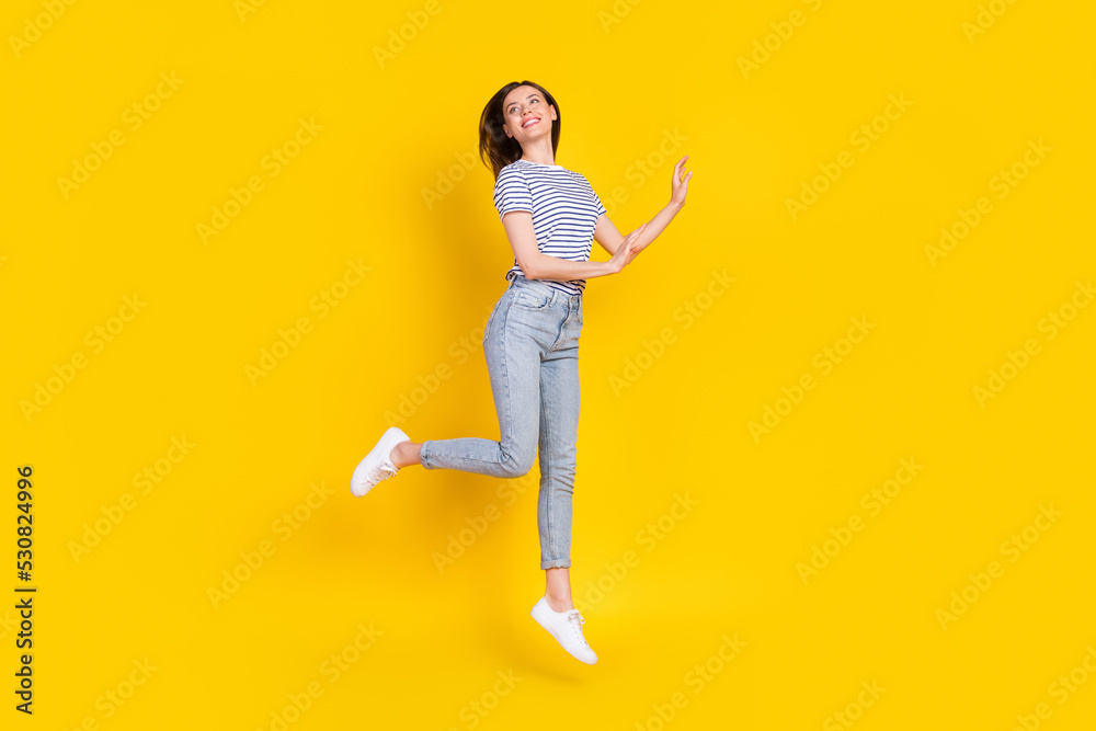 Full size photo of adorable young lady look empty jumping feel free dressed trendy striped clothes isolated on yellow color background