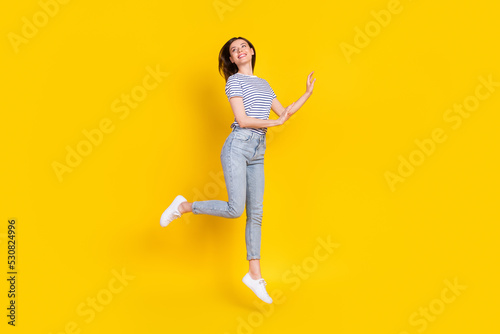 Full size photo of adorable young lady look empty jumping feel free dressed trendy striped clothes isolated on yellow color background