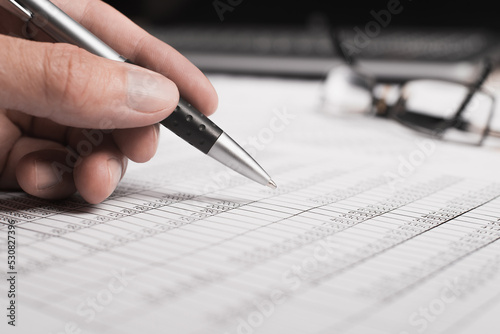 Close-up of an office worker's hand holding a pen, bills documents and eyeglasses, selective focus. Investment, business and finance, accounting concept