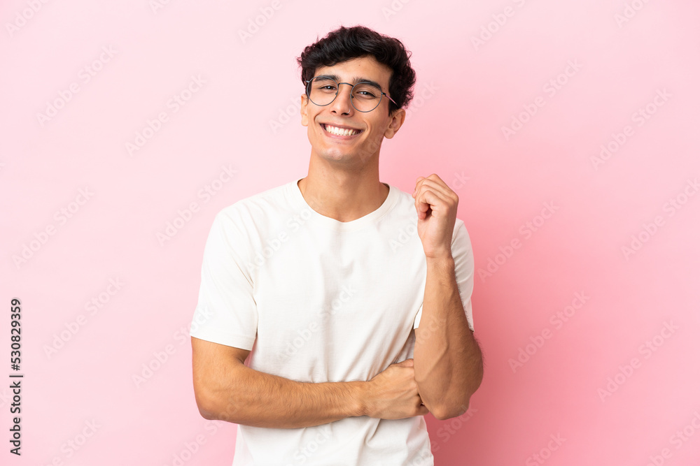 Young Argentinian man isolated on pink background laughing