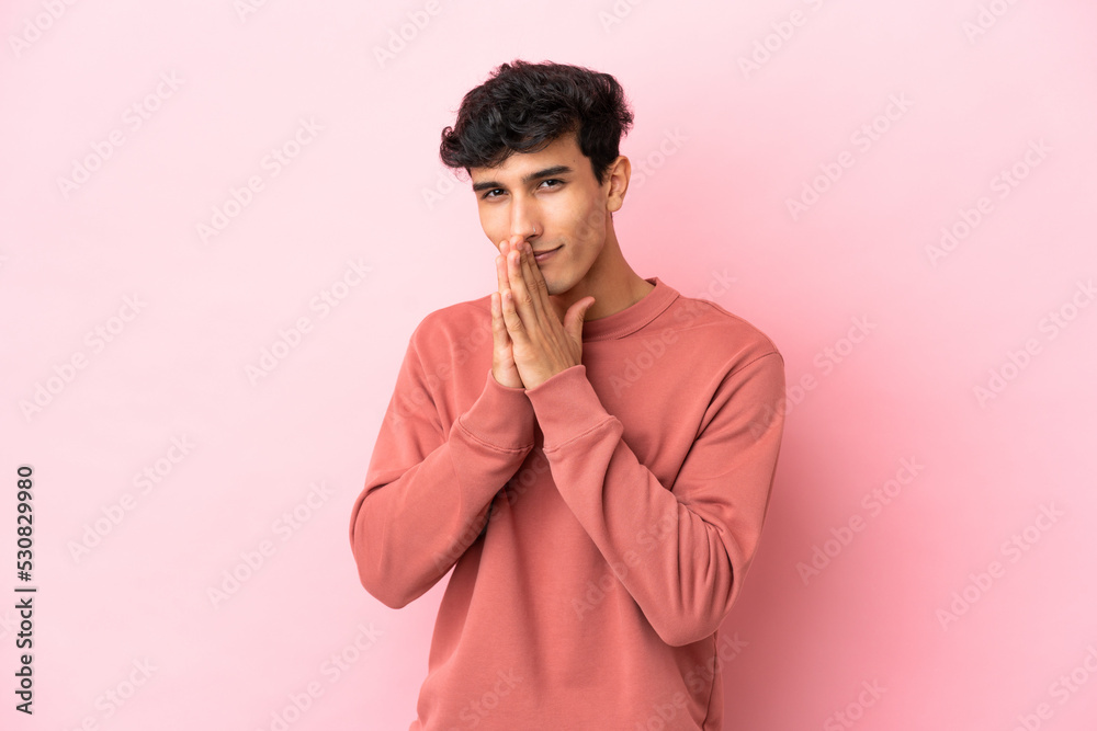 Young Argentinian man isolated on pink background keeps palm together. Person asks for something