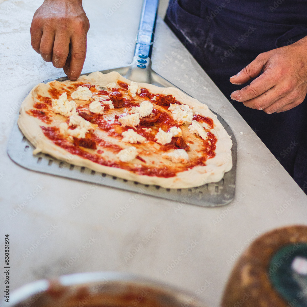 Italian pizza chef preparing and cooking pizza with mozzarella cheese tomato sauce and fresh basil leaf