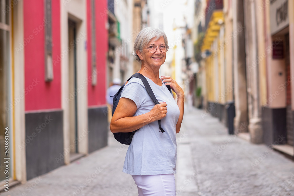Attractive smiling elderly woman walking in the narrow streets of Seville, Spain, elderly traveler with backpack visiting the old town Attractive smiling elderly woman walking in the narrow streets of Seville, Spain, elderly traveler with backpack visiting the old town