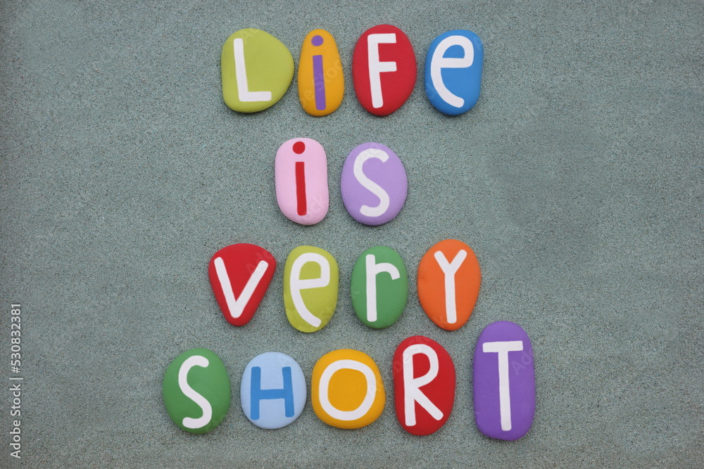 Obraz premium Life is very short, creative message composed with multi colored stone letters over green sand