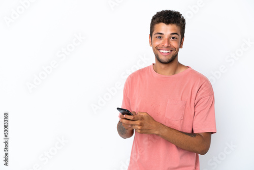 Young handsome Brazilian man isolated on white background sending a message with the mobile