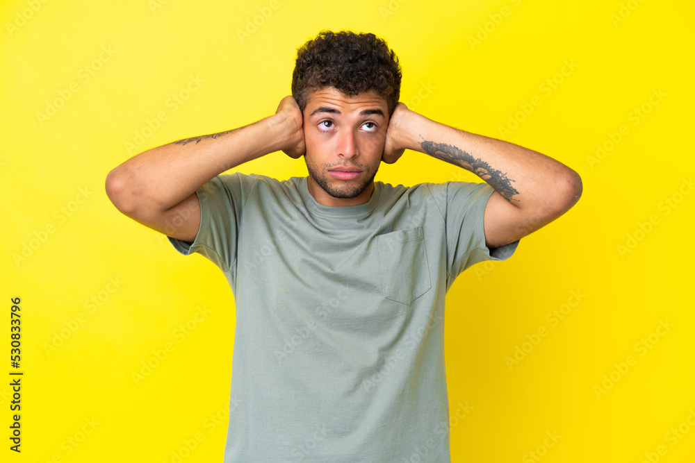 Young handsome Brazilian man isolated on yellow background frustrated and covering ears Young handsome Brazilian man isolated on yellow background frustrated and covering ears