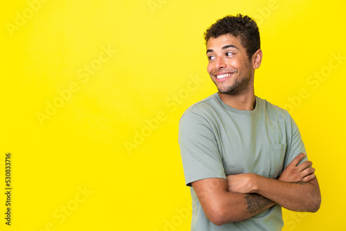 Young handsome Brazilian man isolated on yellow background looking to the side and smiling