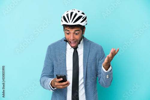 Young business Brazilian man with bike helmet isolated on blue background surprised and sending a message © luismolinero