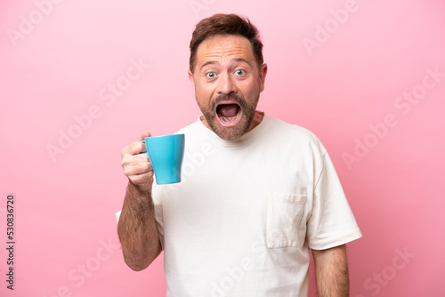 Middle age caucasian man holding cup of coffee isolated on pink background with surprise and shocked facial expression