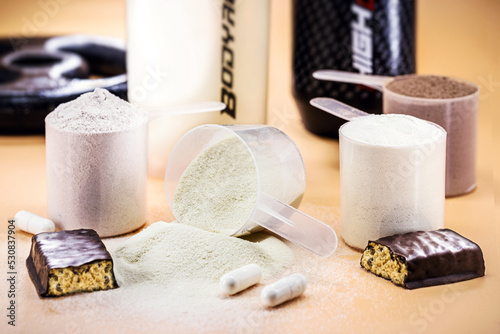 spoons with Creatine, whey and casein, amino acid pills, food supplements and protein bar for physical exercises, gym in the background, muscle mass gain