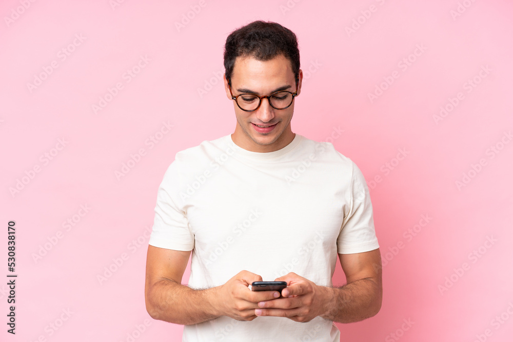 Young caucasian man isolated on pink background sending a message with the mobile Young caucasian man isolated on pink background sending a message with the mobile