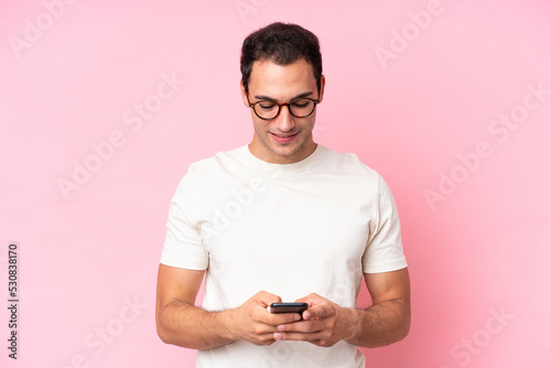 Young caucasian man isolated on pink background sending a message with the mobile © luismolinero