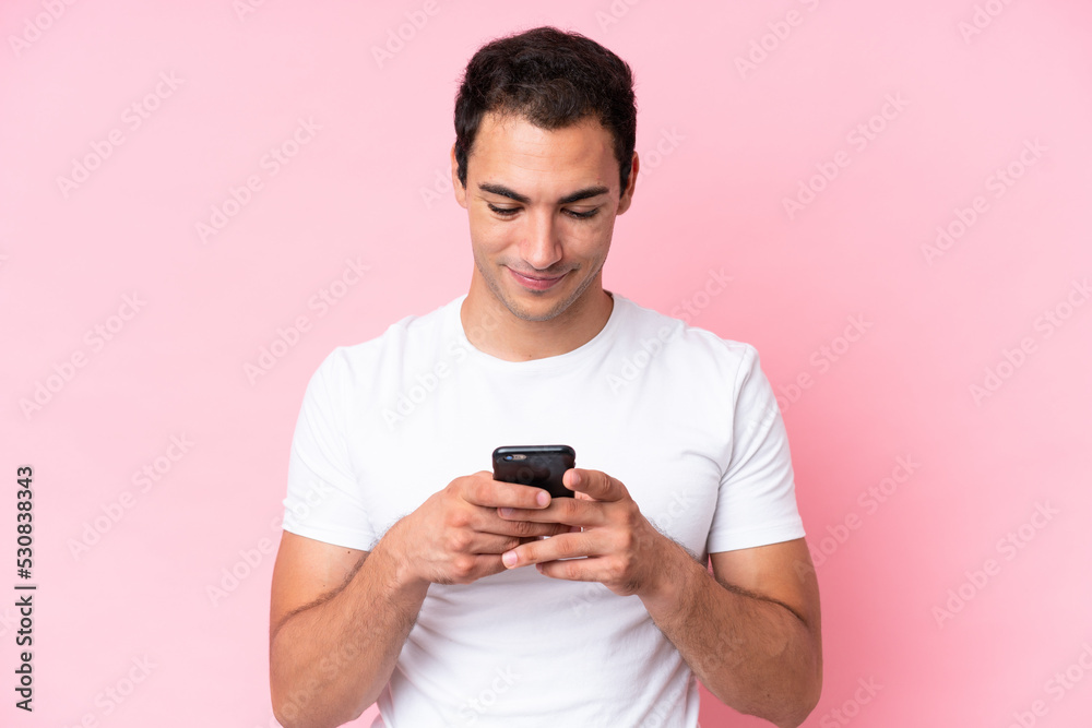 Young caucasian man isolated on pink background using mobile phone Young caucasian man isolated on pink background using mobile phone
