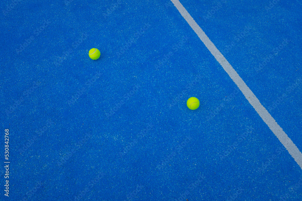 two paddle tennis balls on a blue artificial grass court near the centre line. Racket sports