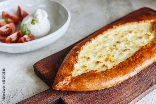 Traditional Turkish baked pide dish. Middle Eastern snacks. Turkish pizza. Turkish pide with cheese - Kasarli Pide and tomatoes with burrata cheese on grey concrete background. Selective focus
