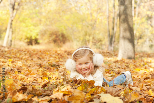 Happy girl portrait lying on autumn maple leaves and smiling in autumn park