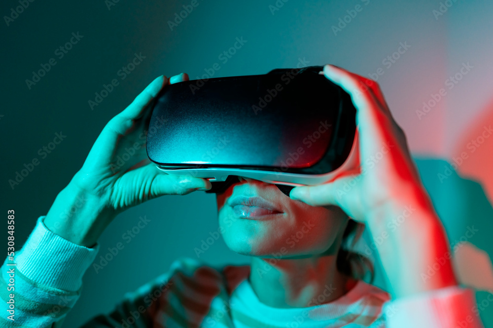 Opportunities in virtual reality. Amazed European woman testing modern high-tech helmet, getting 3D experience at home. Joyful young female in VR headset watching videos and movies. Neon light. 