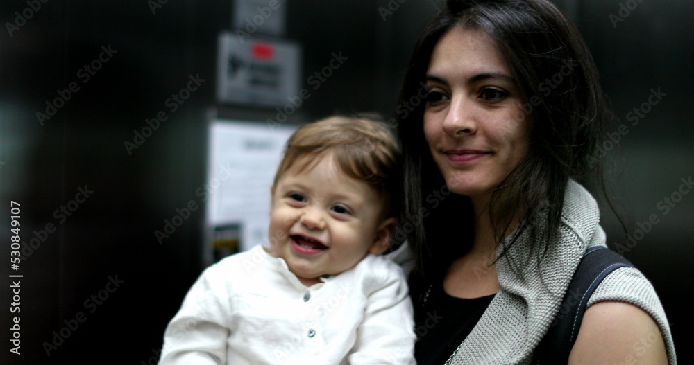 Playful mother holding baby infant insidde elevator interaction with mirror Playful mother holding baby infant insidde elevator interaction with mirror