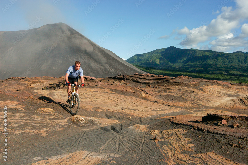 Fototapeta premium Western tourist riding a mountain bike on Yasur Volcano, Tanna Island, Vanuatu